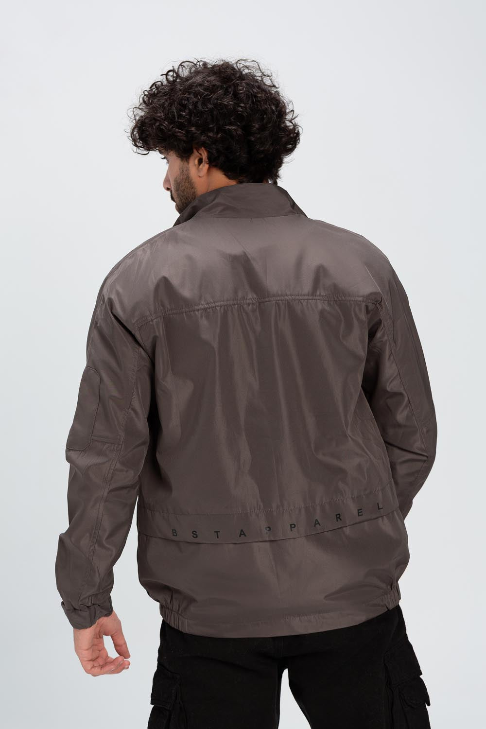 Rear view of a man wearing a brown waterproof jacket with a printed logo band across the back.