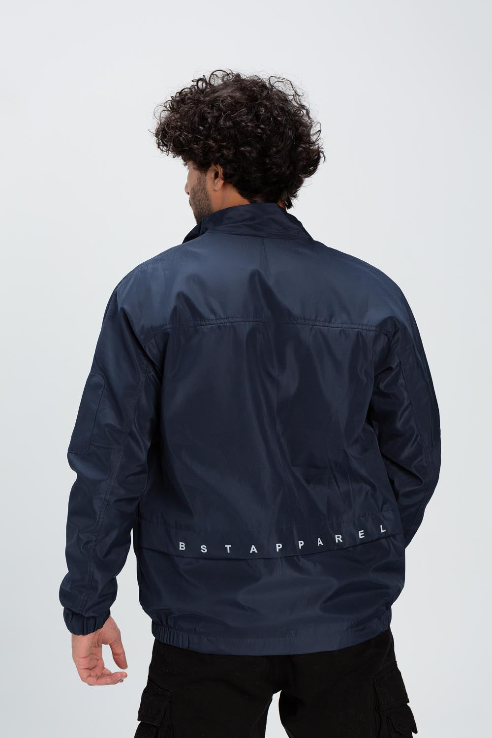 Rear view of a man wearing a navy blue waterproof jacket with white text printed on the back hem.