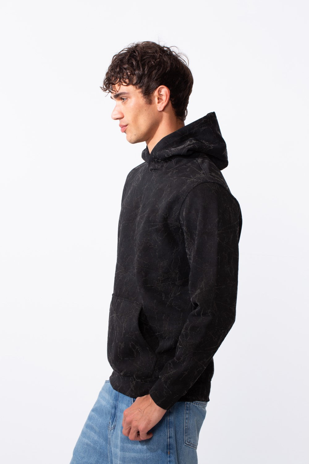 A man in profile wears a black tie-dye slim fit long sleeve hoodie and blue jeans.
