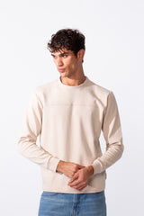 A man wears a plain, cream-colored slim fit round neck sweatshirt with blue jeans.