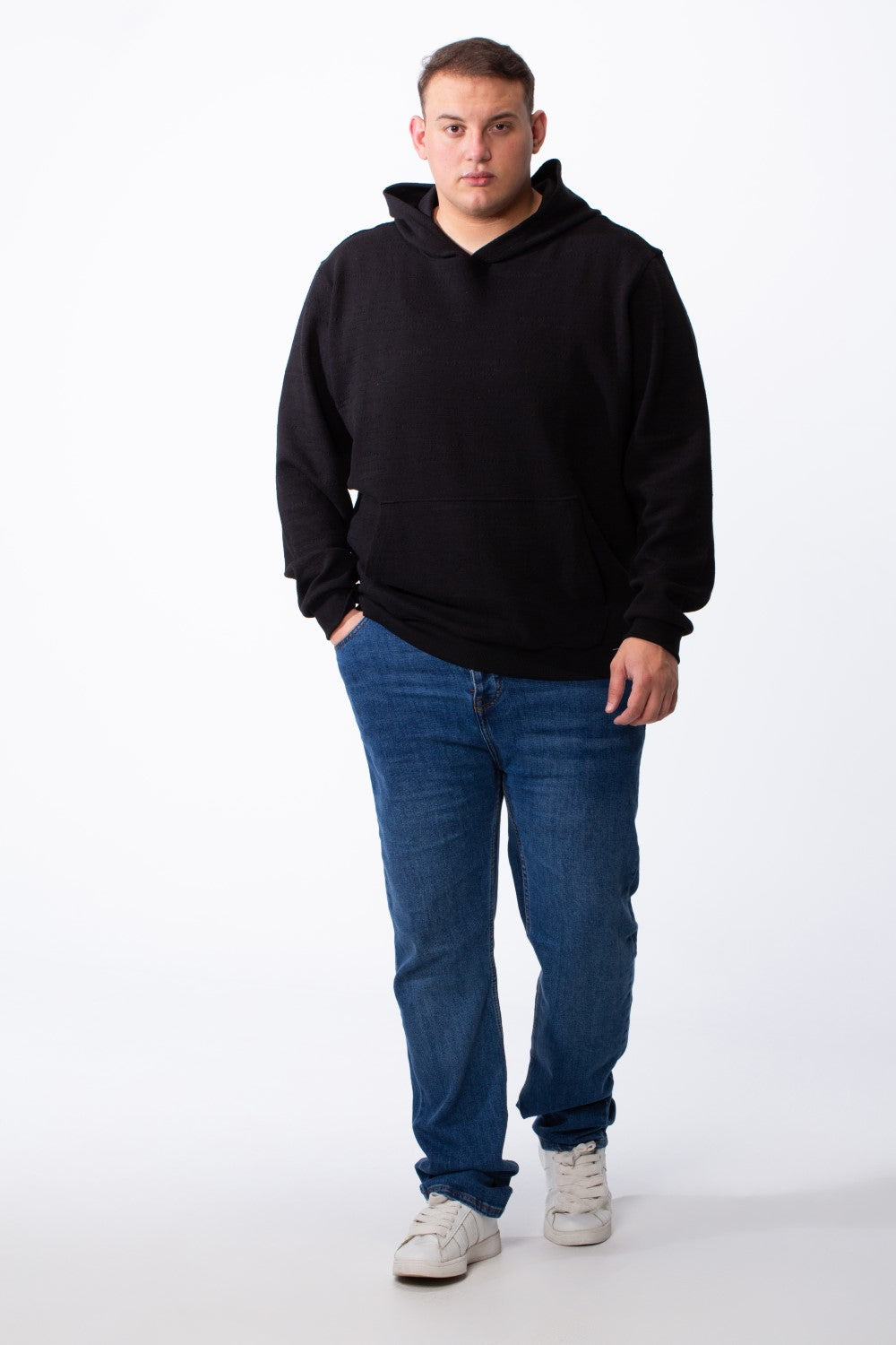A man wears a black long-sleeve big size hoodie with a kangaroo pocket and blue jeans.
