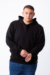 A man wearing a black long-sleeve big size hoodie with a kangaroo pocket and blue jeans.