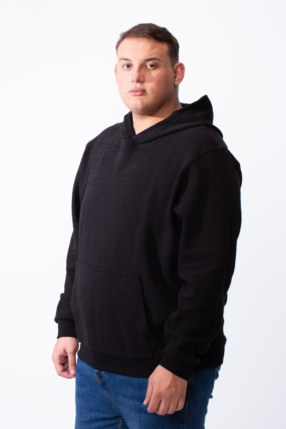A man wearing a black big size long sleeve hoodie with a kangaroo pocket and blue jeans.