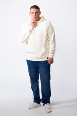 A man wears a cream-colored big size hoodie with a kangaroo pocket and blue jeans.