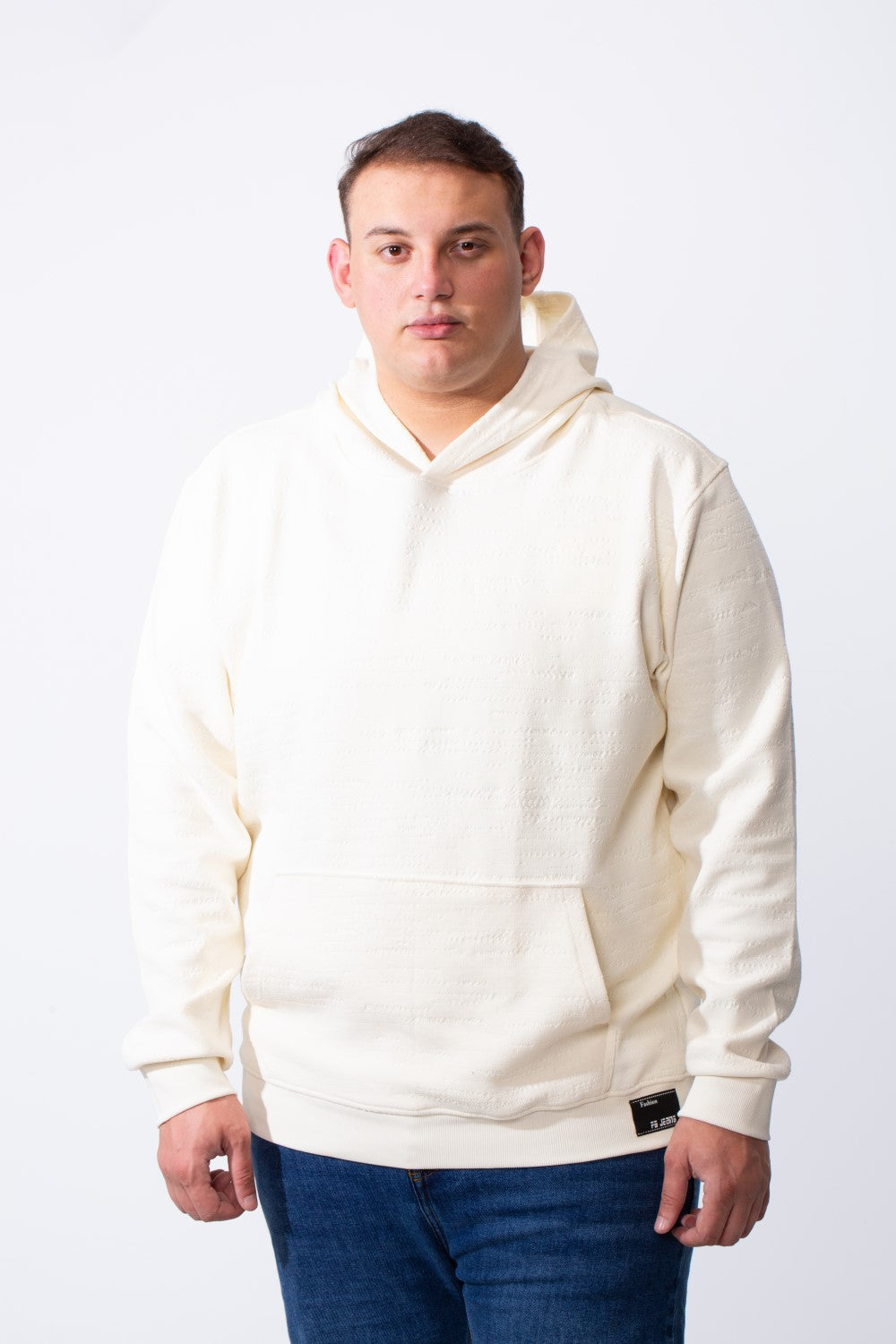 A man wears a cream-colored big size hoodie with a kangaroo pocket and long sleeves.