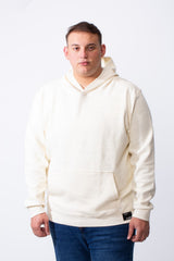 A man wears a cream-colored big size hoodie with a kangaroo pocket and long sleeves.