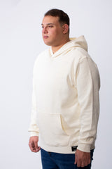 A man wears a cream-colored, long-sleeve big size hoodie with a kangaroo pocket and textured fabric.