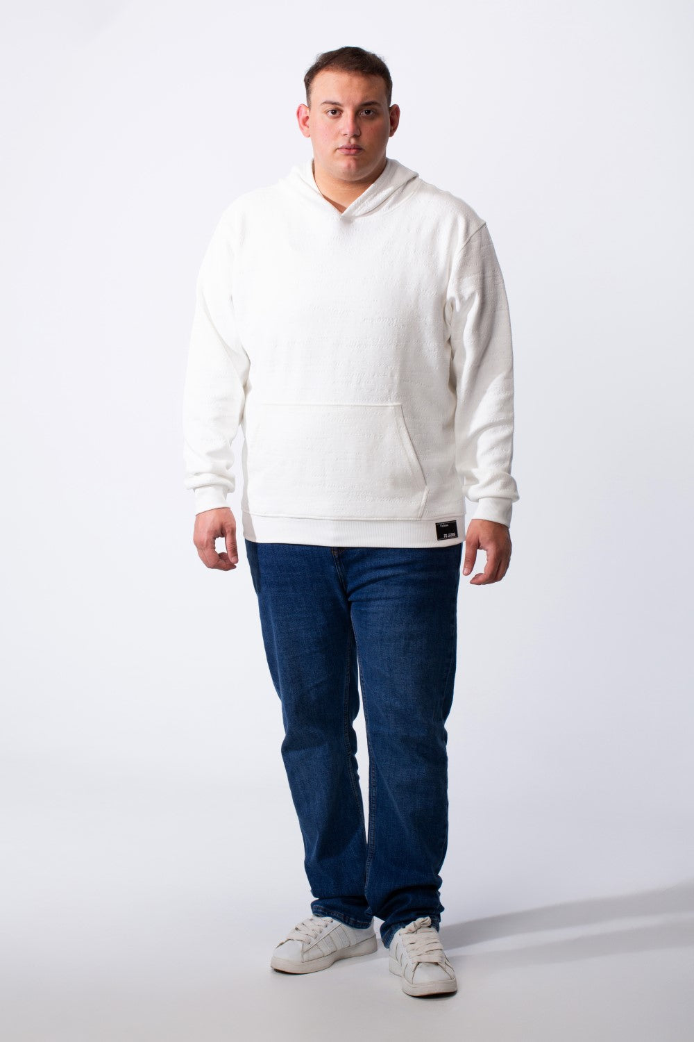 A man wears a white long-sleeve big size hoodie with a kangaroo pocket and blue jeans.