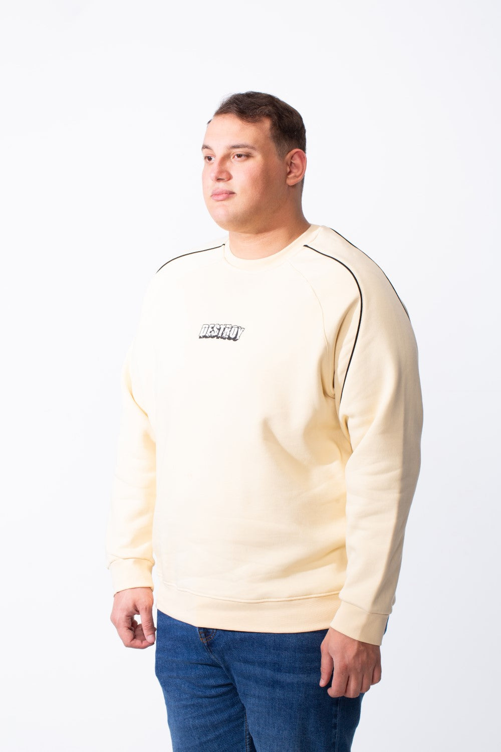 A man wears a cream-colored big size melton sweatshirt with black piping and a crew neck.