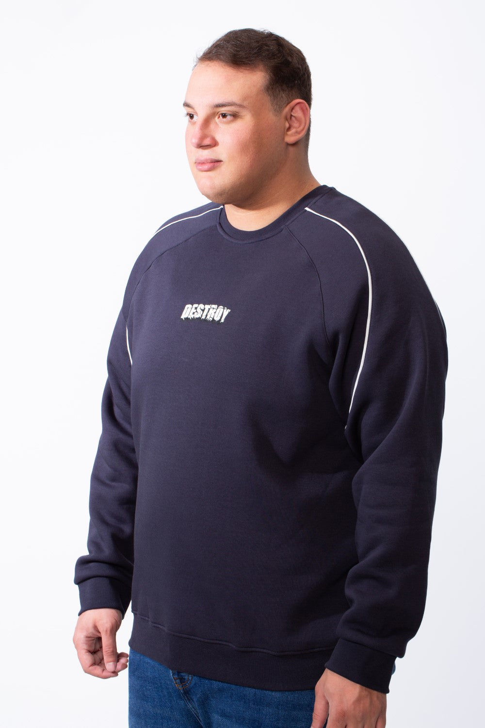 A man wears a navy blue big size crew neck sweatshirt with white piping and a small chest graphic.