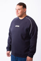 A man wears a navy blue big size crew neck sweatshirt with white piping and a small chest graphic.