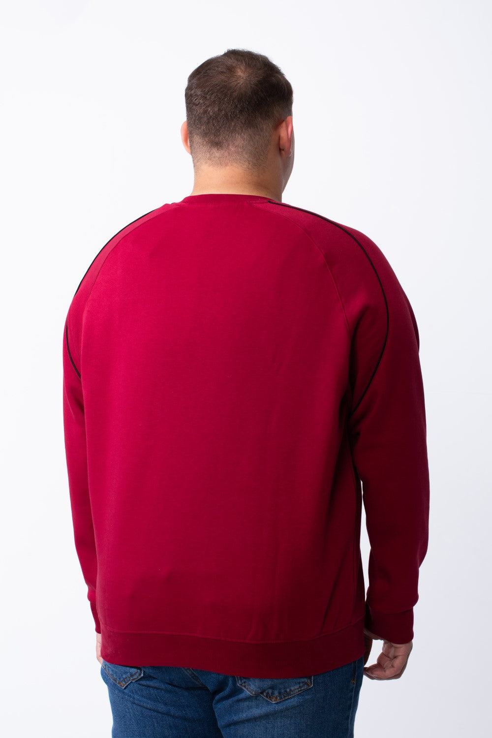 Rear view of a man wearing a big size burgundy crew neck sweatshirt with black piping on the shoulders.