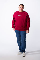 A man wears a big size red crew neck sweatshirt with piping detail and blue jeans.