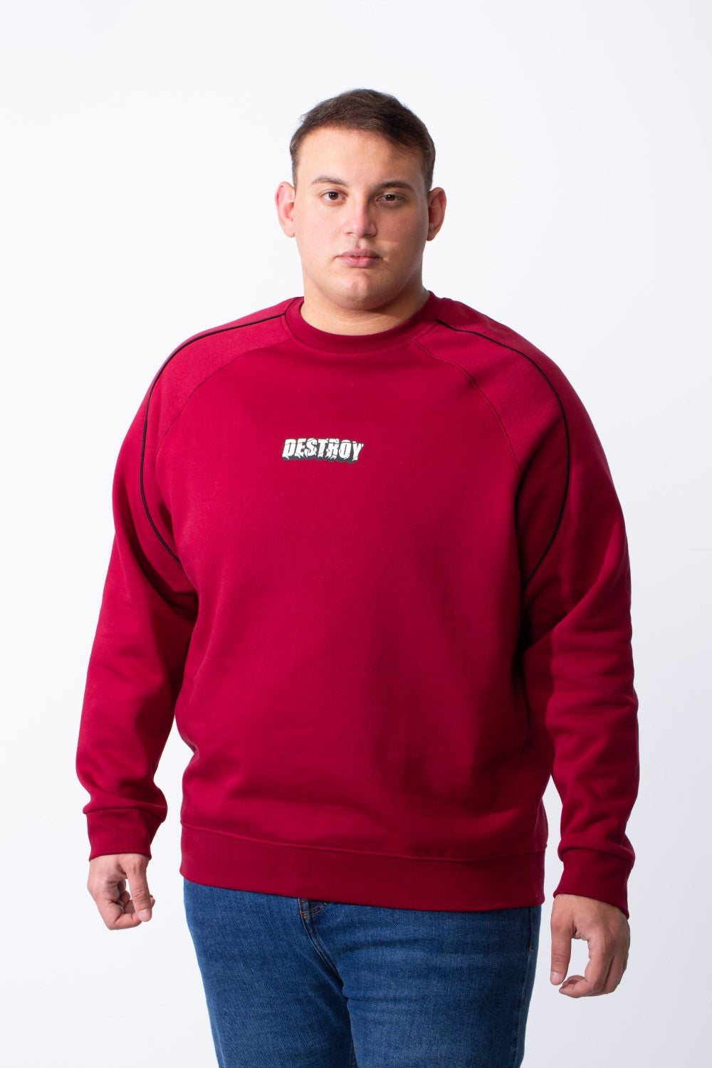 A man wears a big size tomato red crew neck sweatshirt with black piping and a chest graphic.