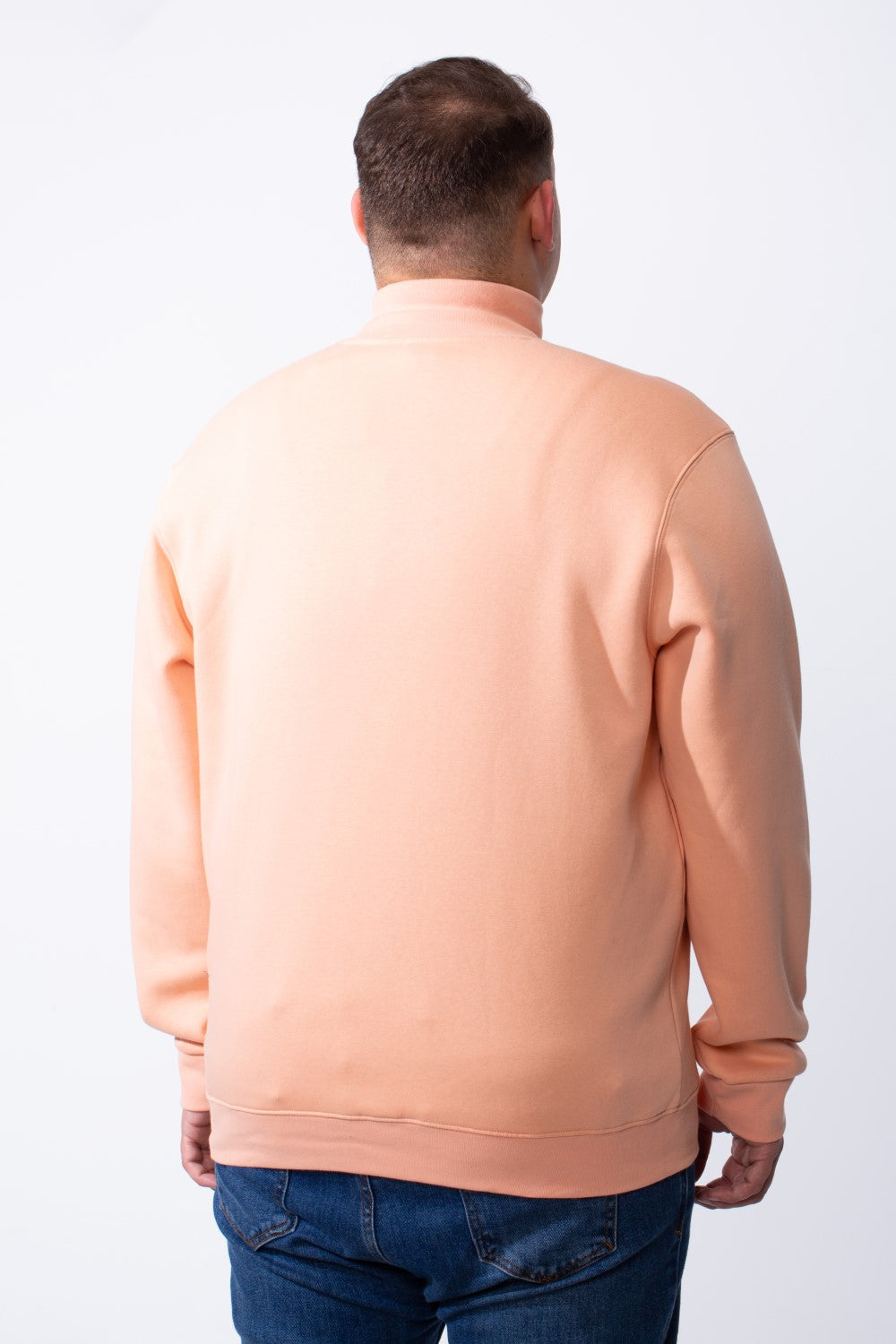Rear view of a man wearing a peach-colored big size mock neck sweatshirt with ribbed cuffs.