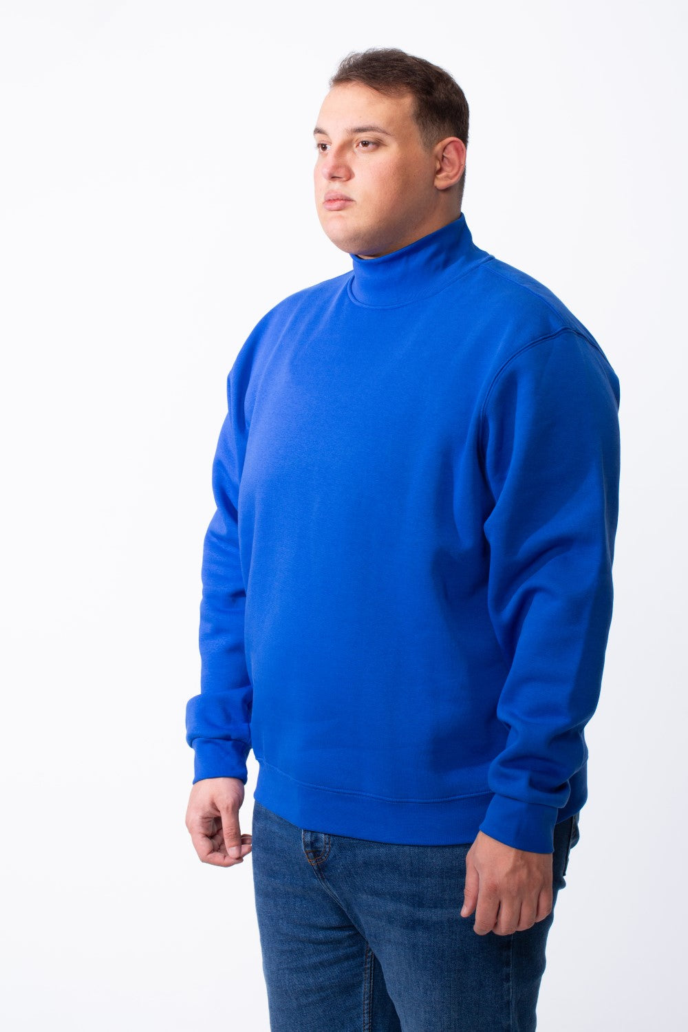 A man wearing a royal blue big size mock neck sweatshirt with ribbed cuffs and blue jeans.