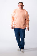 A man wears a peach-colored big size mock neck sweatshirt with ribbed cuffs and blue jeans.