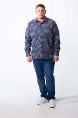 A man wears a big size geometric patchwork button-down shirt in blue with jeans and white sneakers.