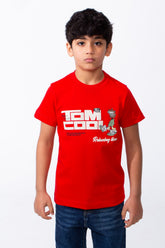 A young boy wears a red ribbed crew neck t-shirt with a white graphic print and blue jeans.