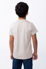 Back view of a boy wearing a light beige ribbed crew neck t-shirt and blue jeans.