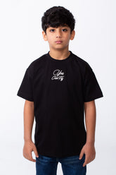 A boy wears a black oversized crew neck t-shirt with white You Can Fly typography embroidery.