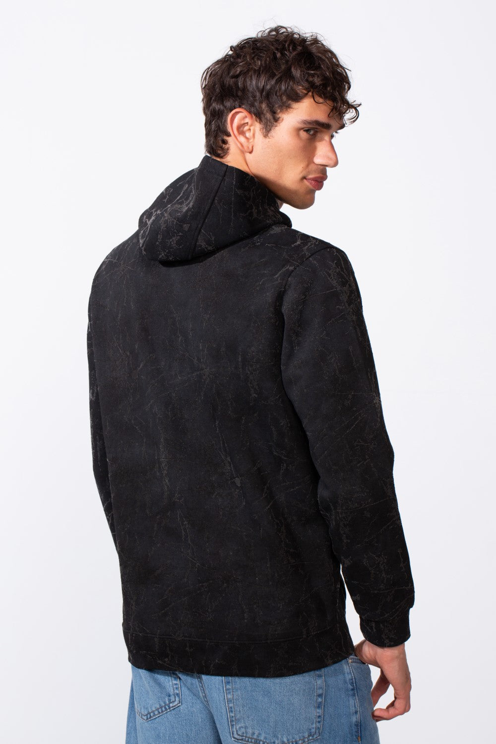 A man from behind wearing a black tie-dye slim fit long sleeve hooded sweatshirt and blue jeans.