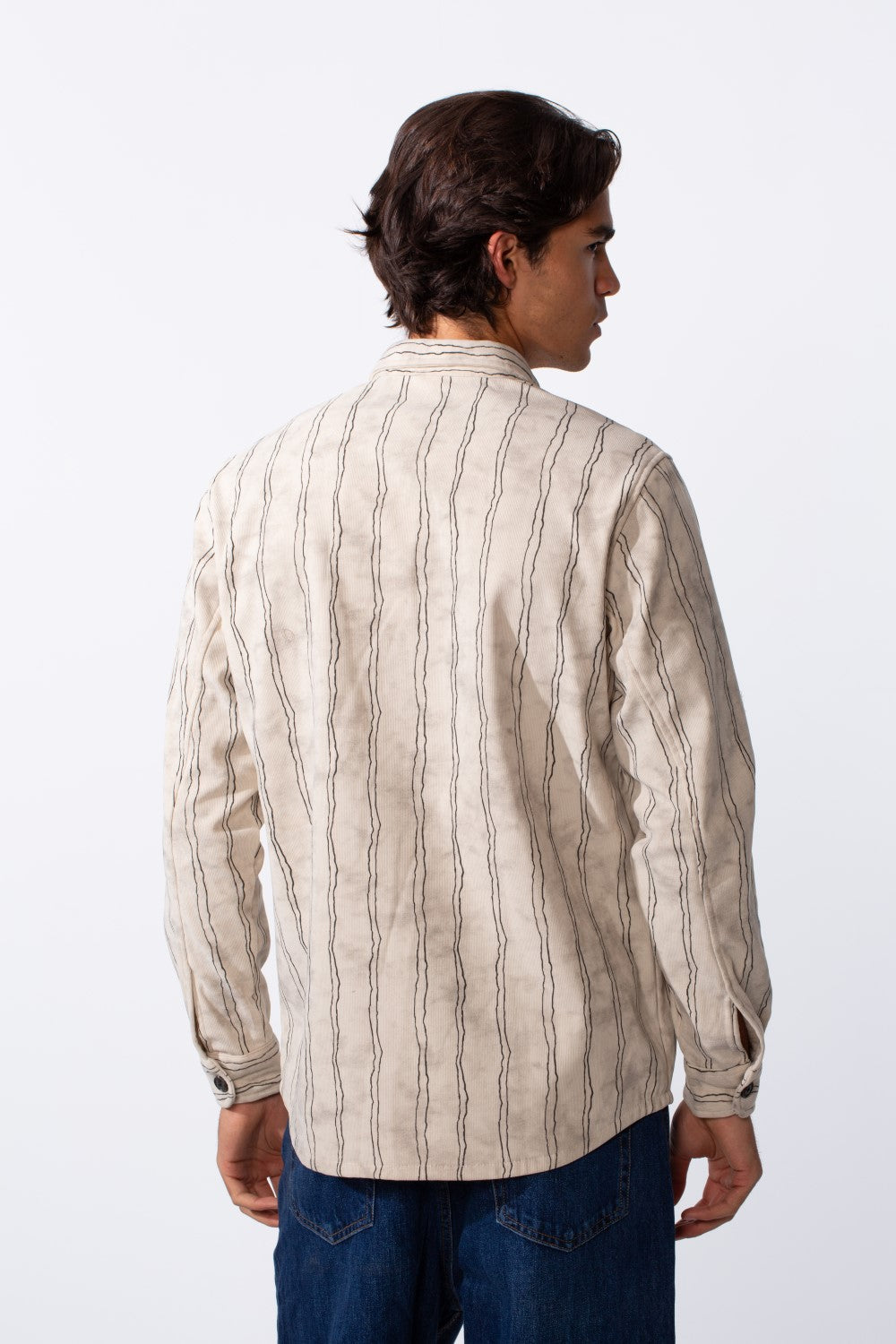 Rear view of a man wearing a slim fit cream velvet shirt with thin vertical black stripes.