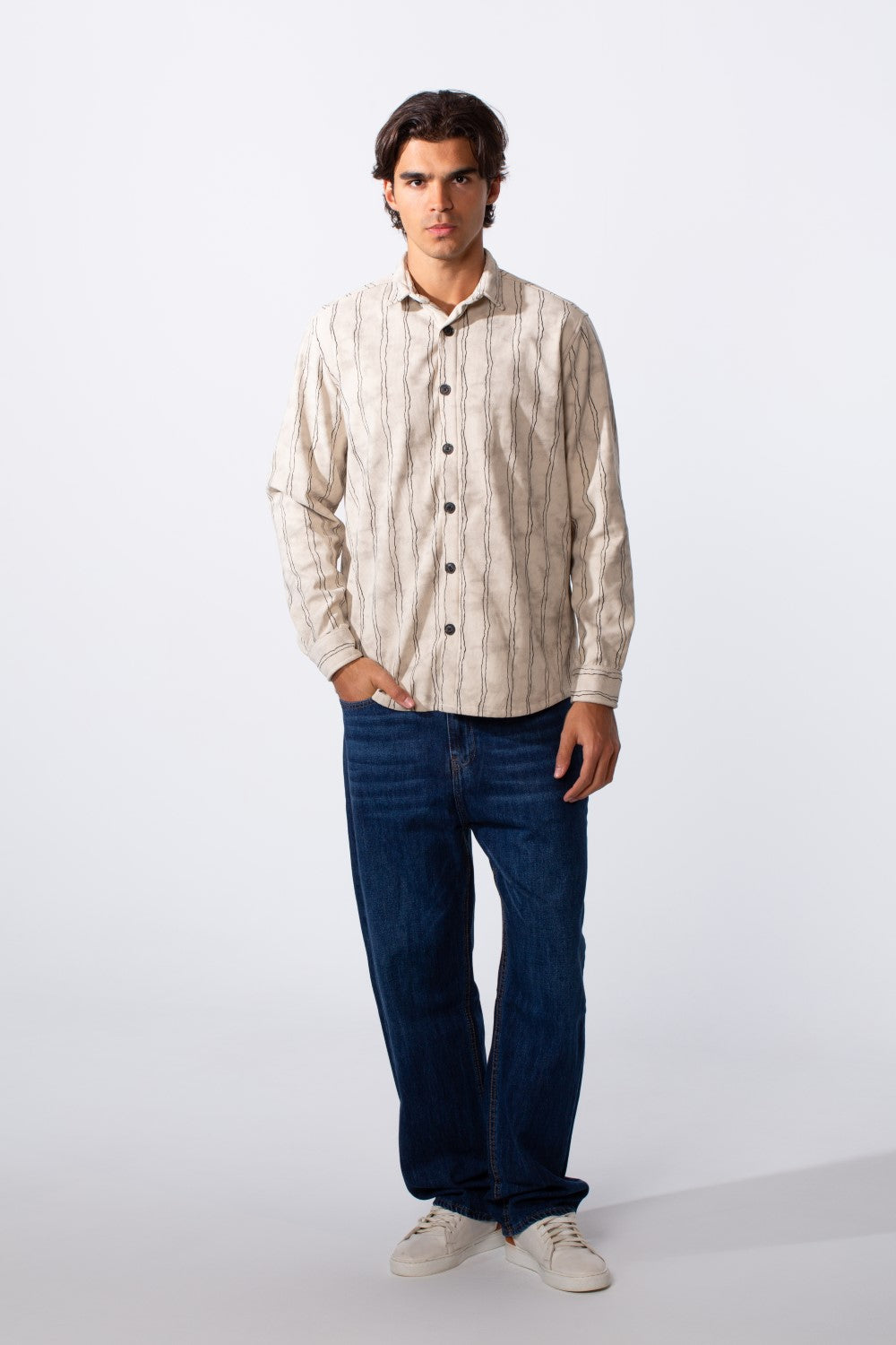 A man models a slim-fit, long-sleeve velvet shirt with vertical stripes and dark blue jeans.