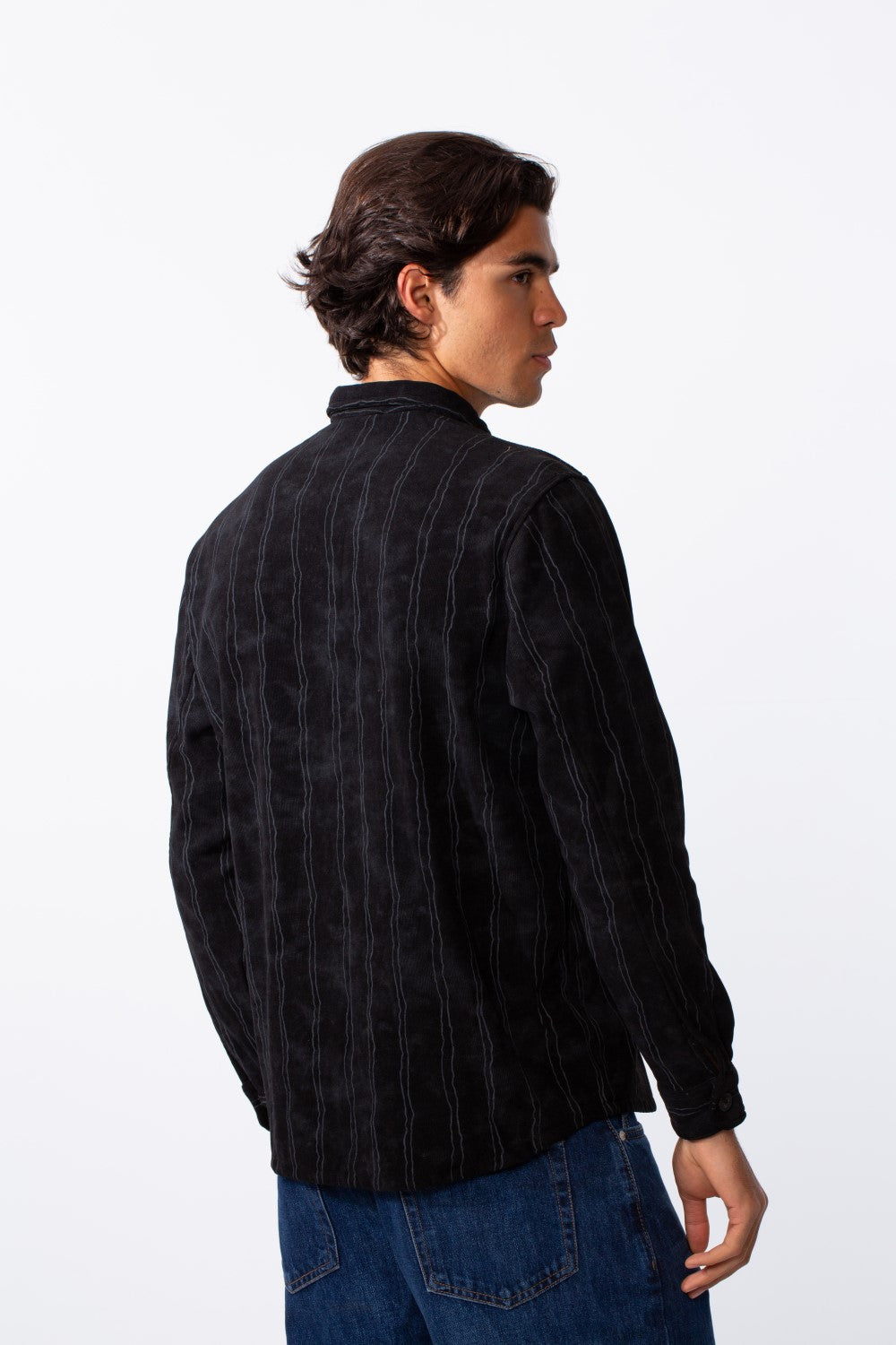 Rear view of a man wearing a black velvet slim fit long sleeve shirt with vertical grey stripes.