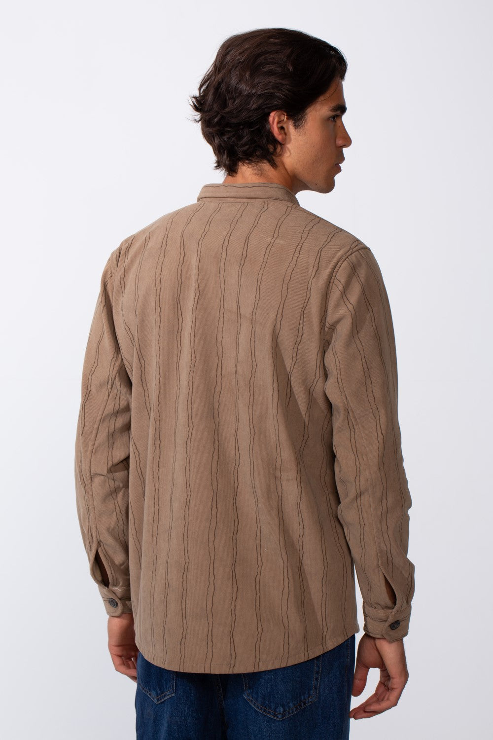 Rear view of a man wearing a tan slim-fit velvet long-sleeve shirt with dark vertical stripes.