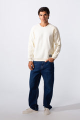 Men's slim fit basic round neck sweatshirt in cream paired with dark blue jeans and white sneakers.