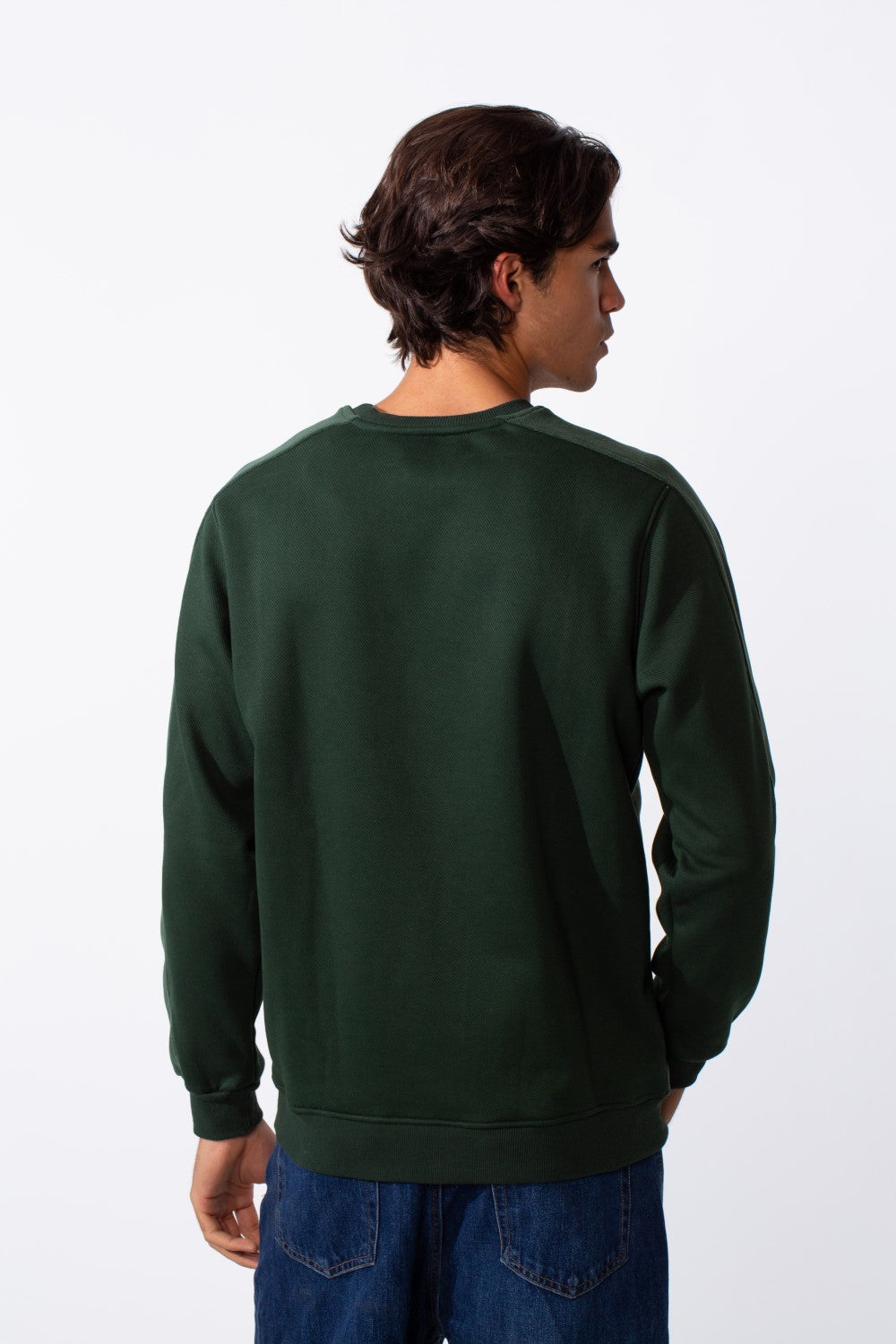 Rear view of a man wearing a dark green slim fit round neck sweatshirt and blue jeans.