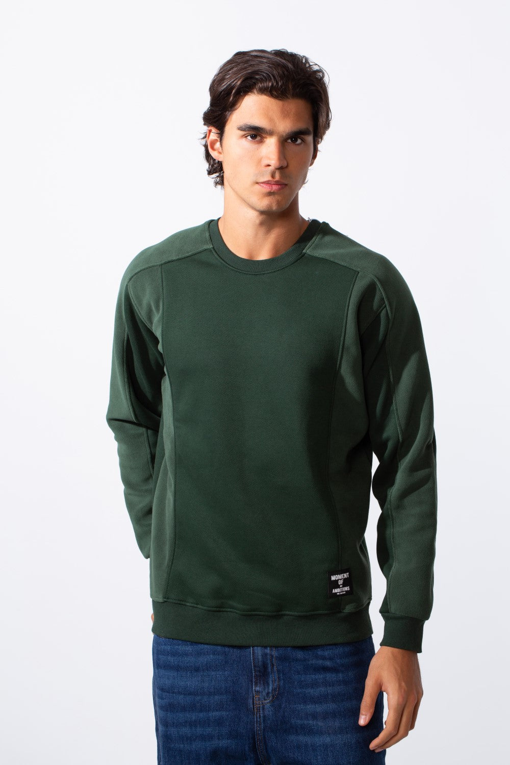 Men's slim fit round neck sweatshirt in dark green with a small logo patch and blue jeans.