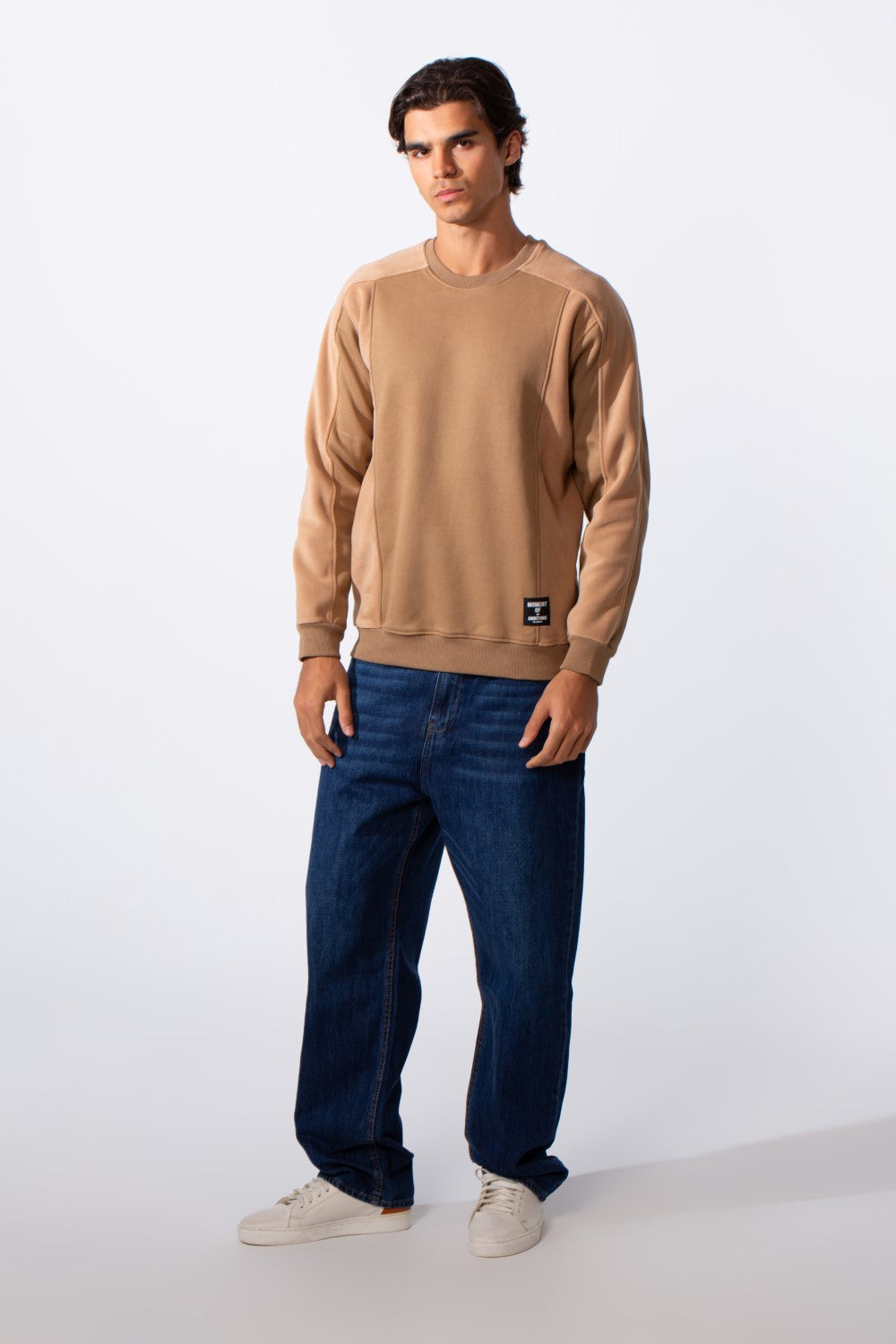 Men's slim fit round neck sweatshirt in tan with blue jeans and white sneakers.