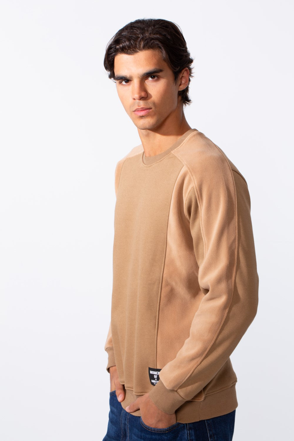 A man wears a tan slim-fit round neck sweatshirt with textured paneling and a small hem tag.