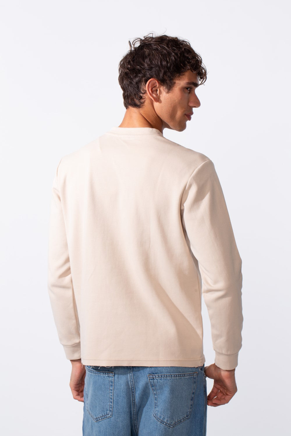 Rear view of a man wearing a plain cream-colored slim fit sweatshirt and blue jeans.