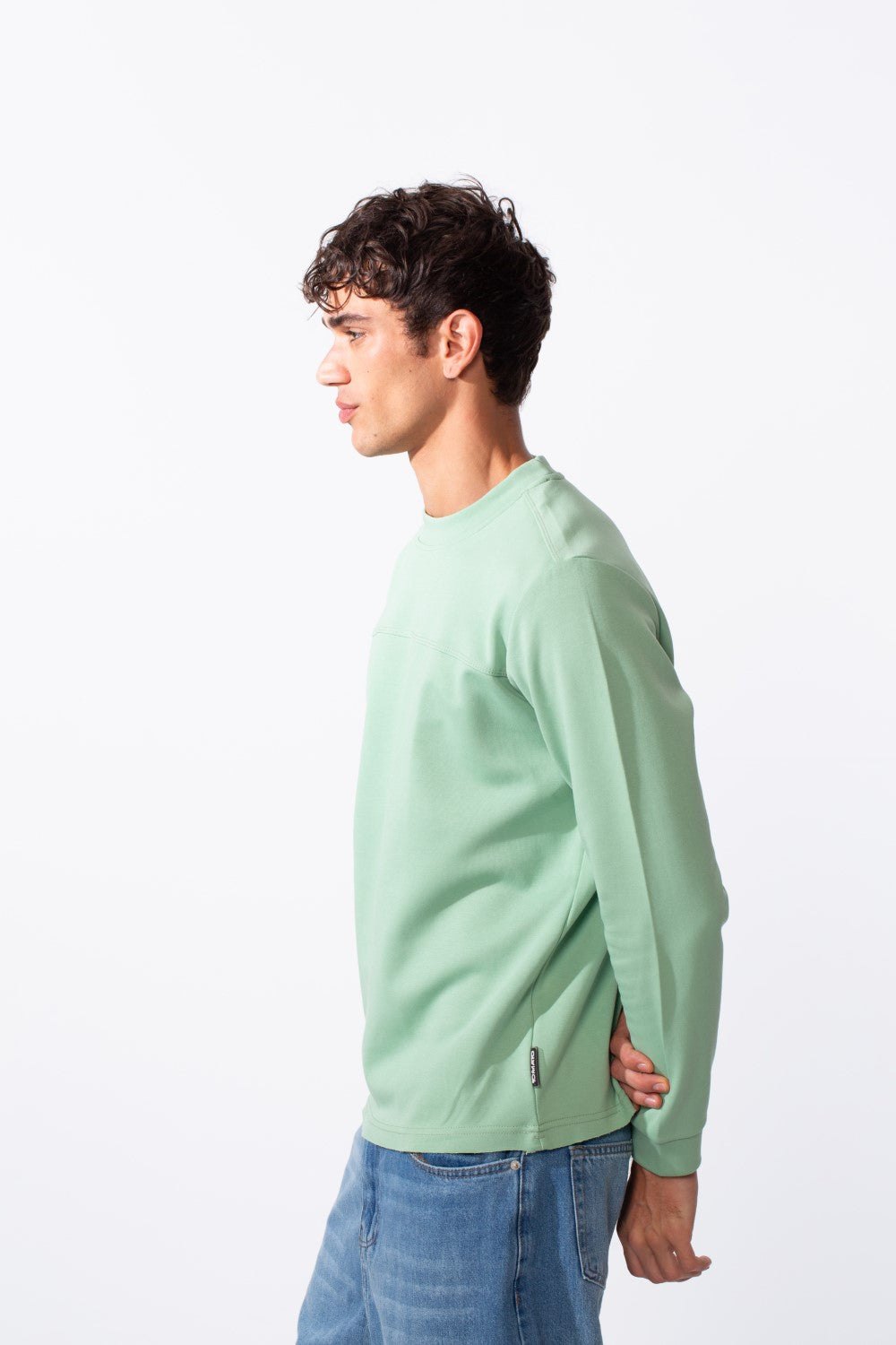 Side profile of a man wearing a light green slim fit round neck sweatshirt and blue jeans.