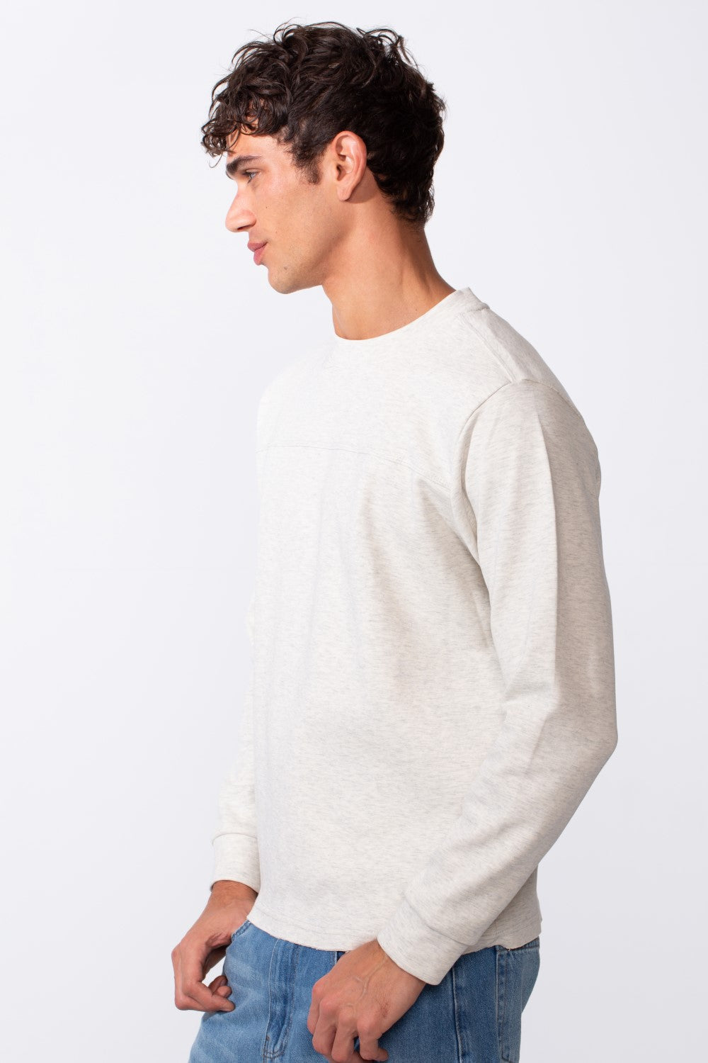 A man in profile wears a light grey, slim-fit round neck sweatshirt with blue jeans.