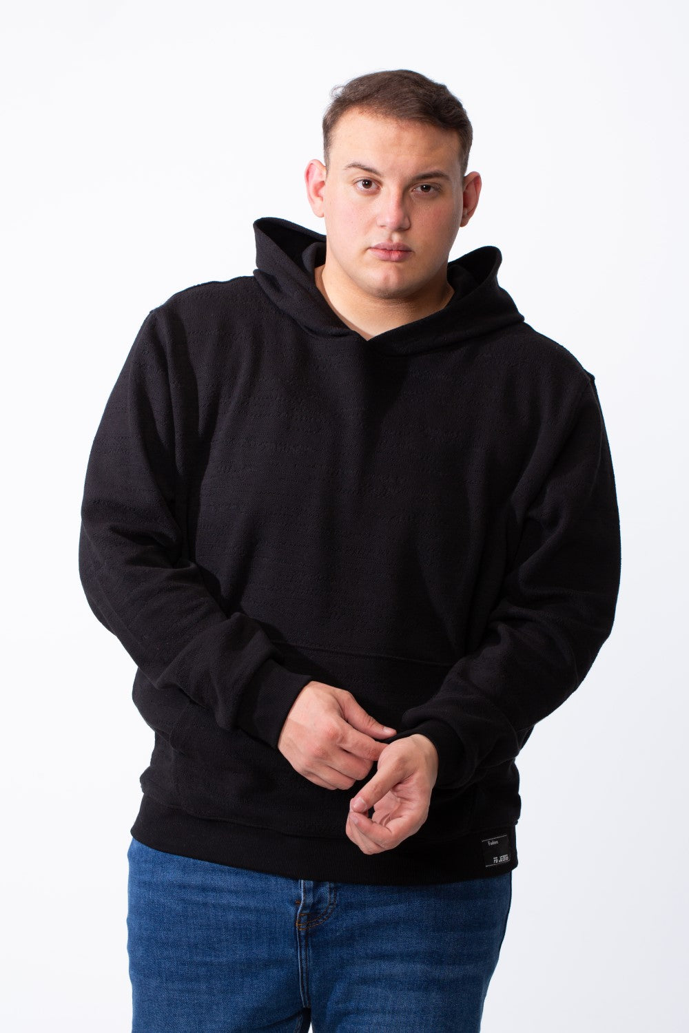 A man wearing a black long-sleeve big size hoodie with a kangaroo pocket and blue jeans.