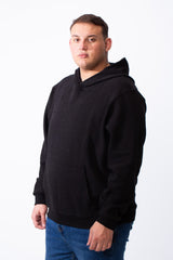A man wearing a black big size long sleeve hoodie with a kangaroo pocket and blue jeans.