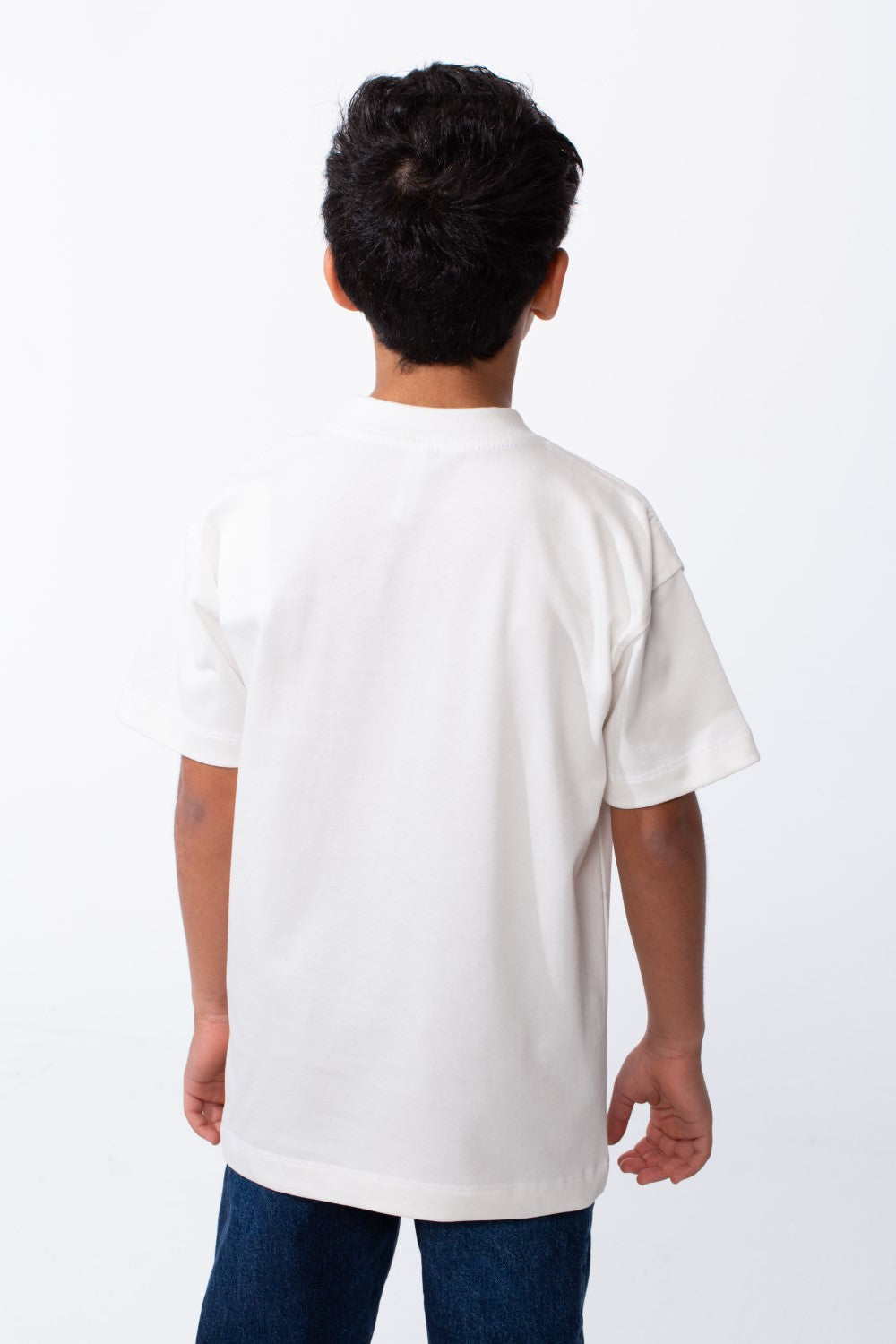 Rear view of a boy wearing a white ribbed crew neck t-shirt and blue jeans.