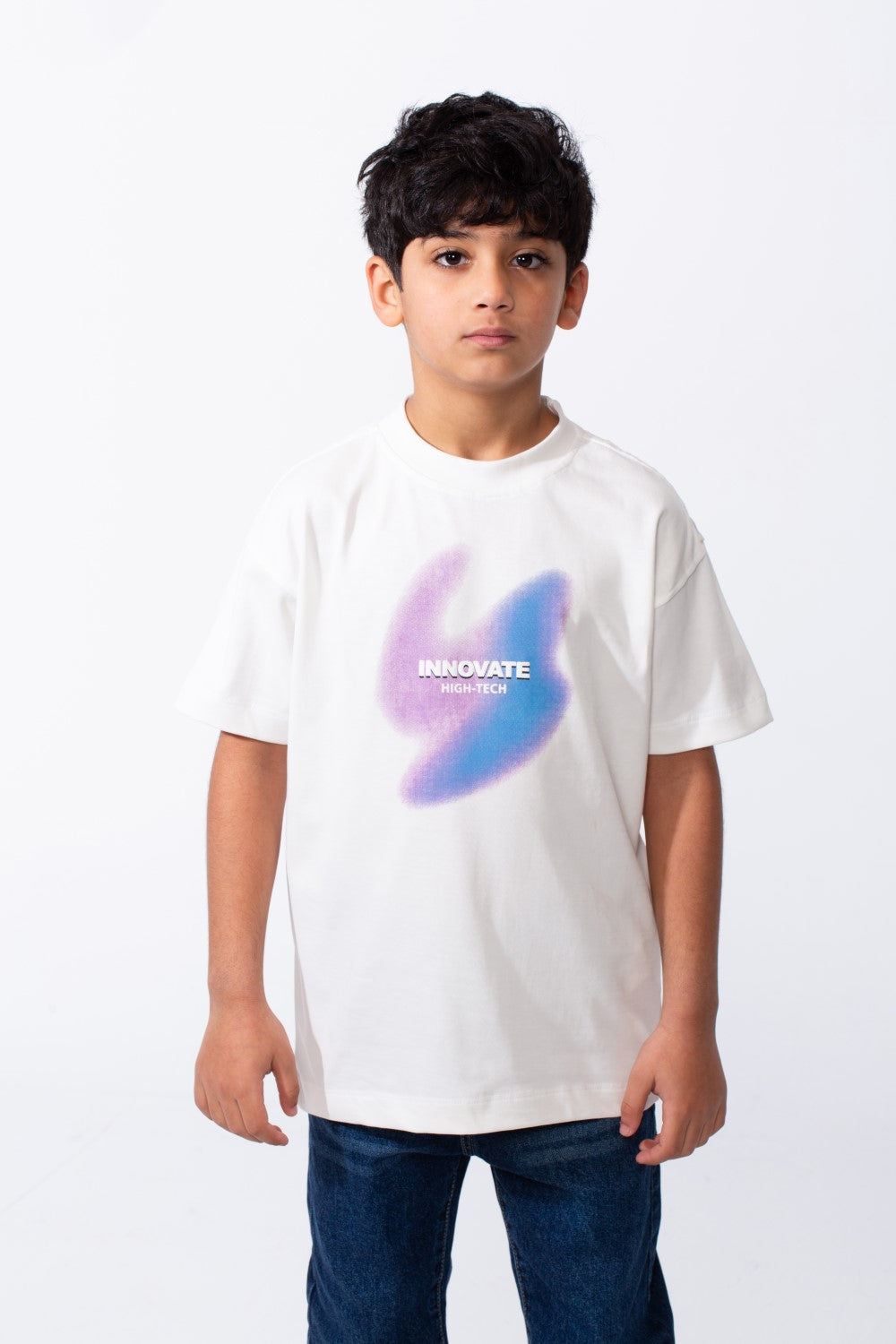 A boy wears a white ribbed crew neck t-shirt with a purple and blue graphic and typography.