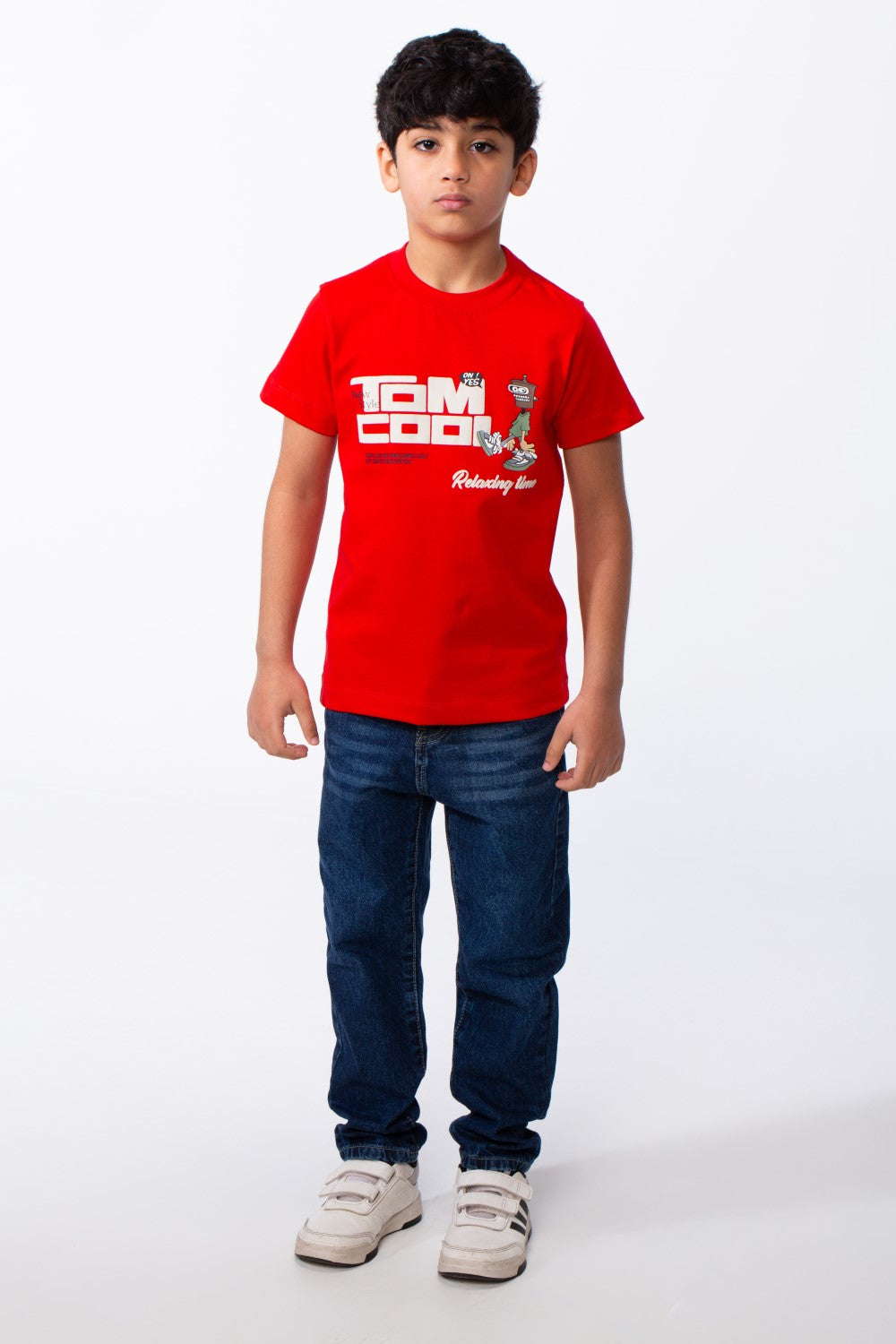 A boy wears a red ribbed crew neck t-shirt with a graphic print and dark blue jeans.