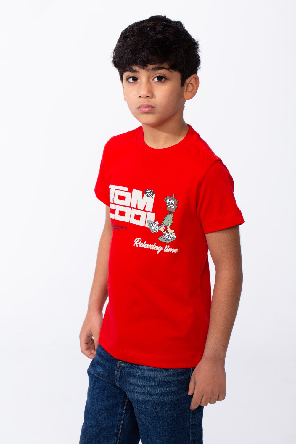 A young boy wears a red ribbed crew neck t-shirt with a playful graphic and blue jeans.