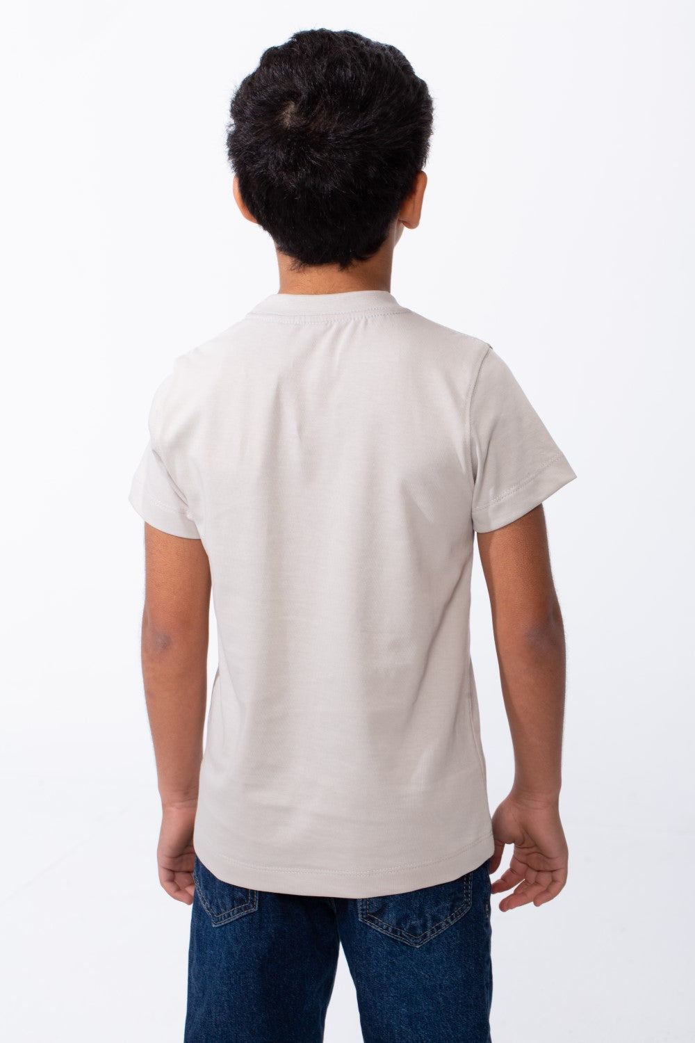 Back view of a boy wearing a light beige ribbed crew neck t-shirt and blue jeans.