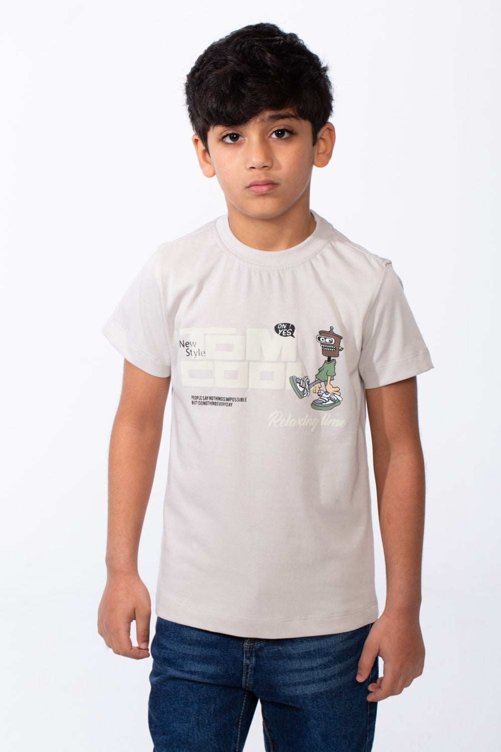 A boy wears a light beige ribbed crew neck t-shirt with a playful graphic and blue jeans.