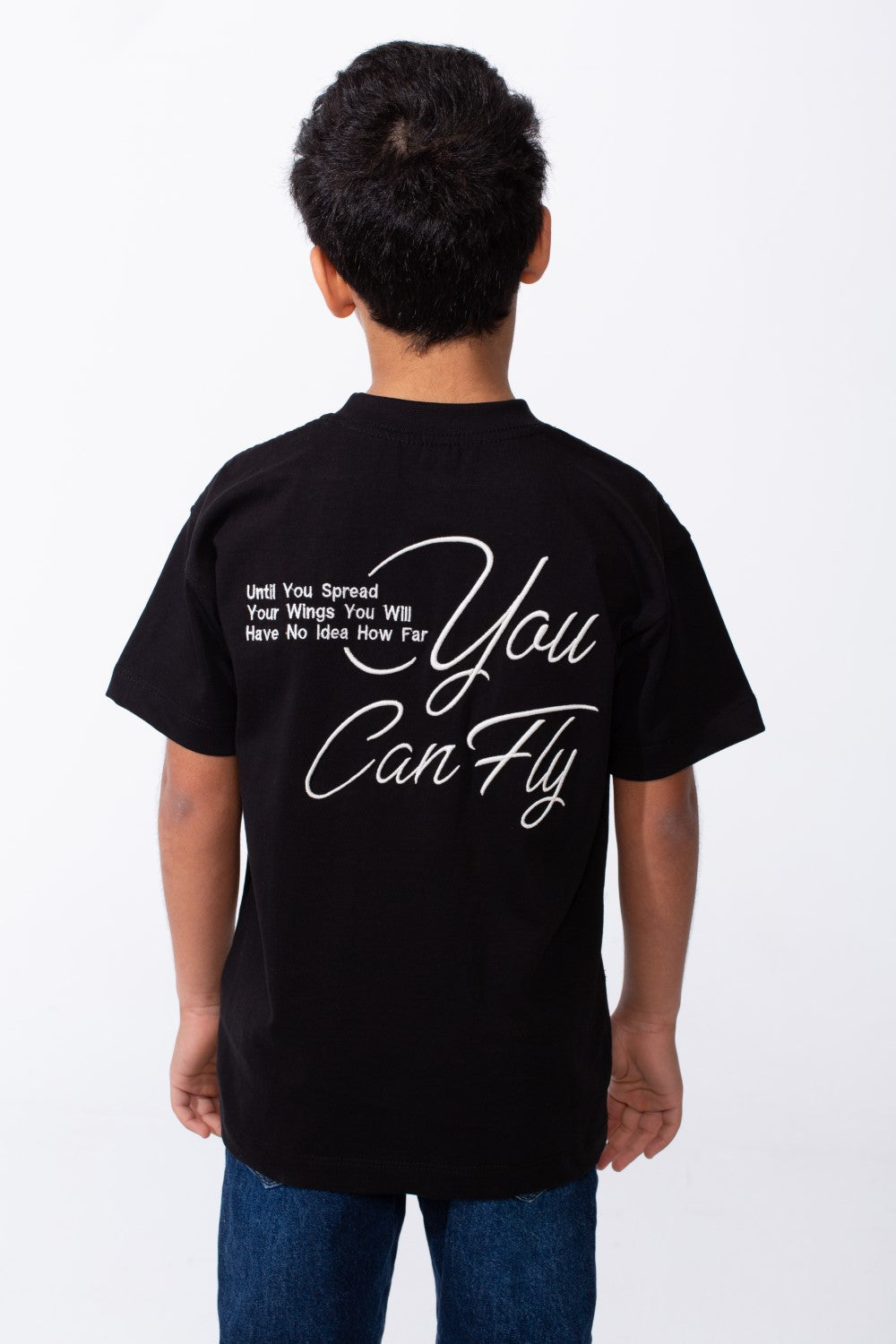 Back view of a boy wearing a black oversized t-shirt with white typography and embroidery.