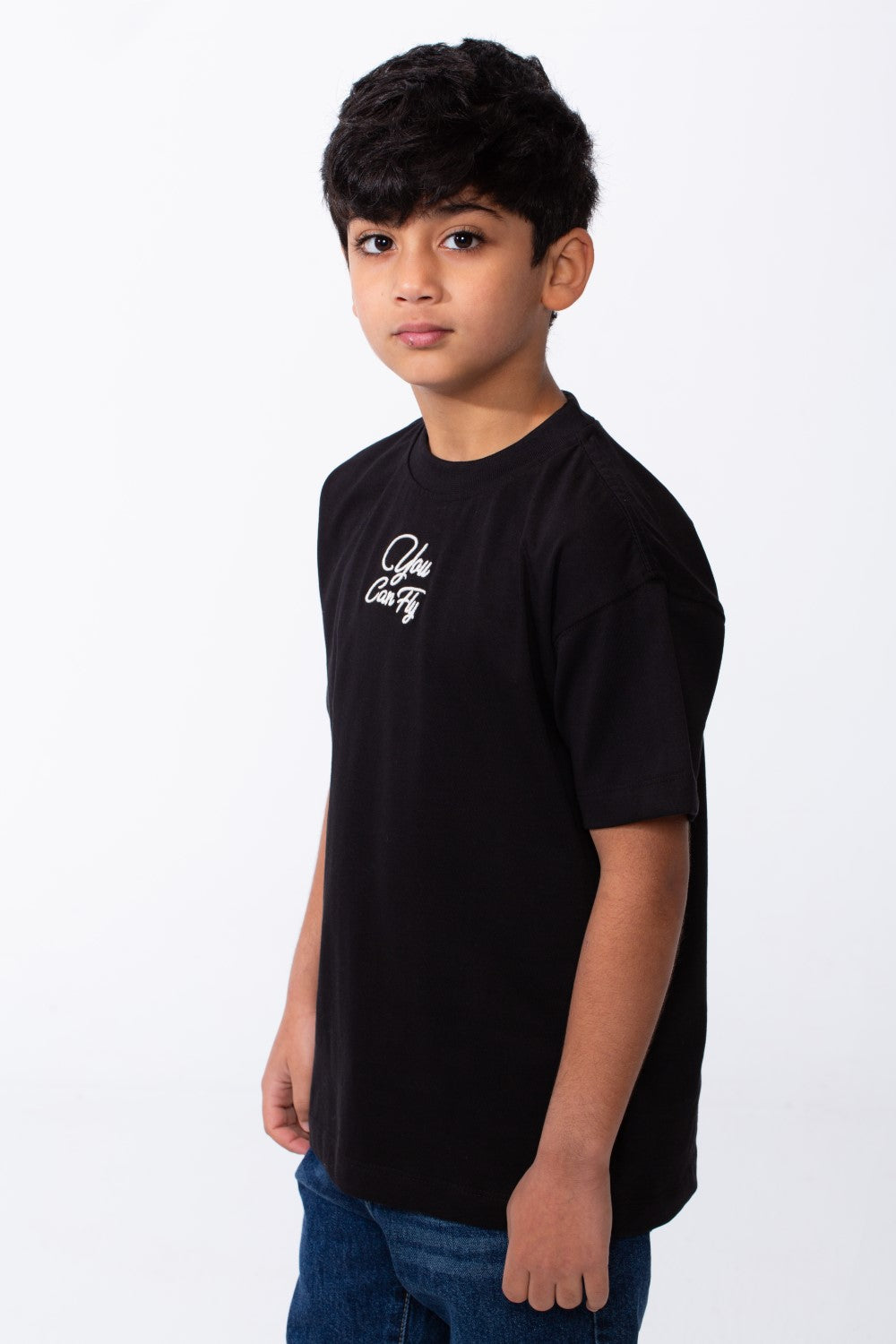 A boy wears a black oversized crew neck t-shirt with white typography embroidery on the chest.