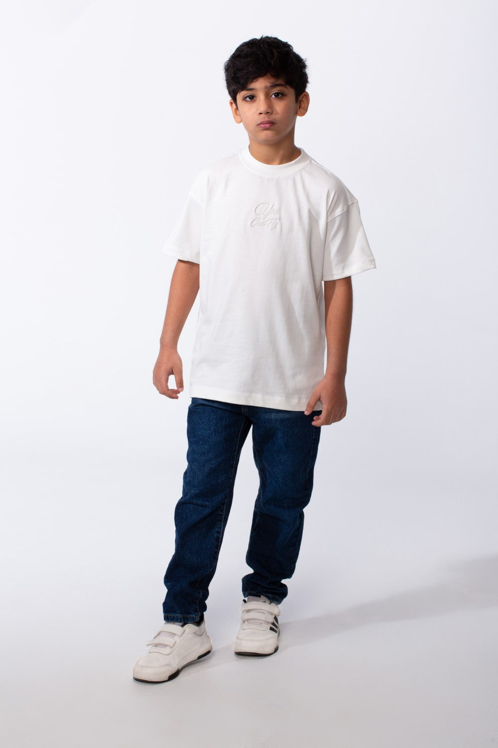 A boy wearing a white oversized crew neck t-shirt with subtle typography embroidery and blue jeans.