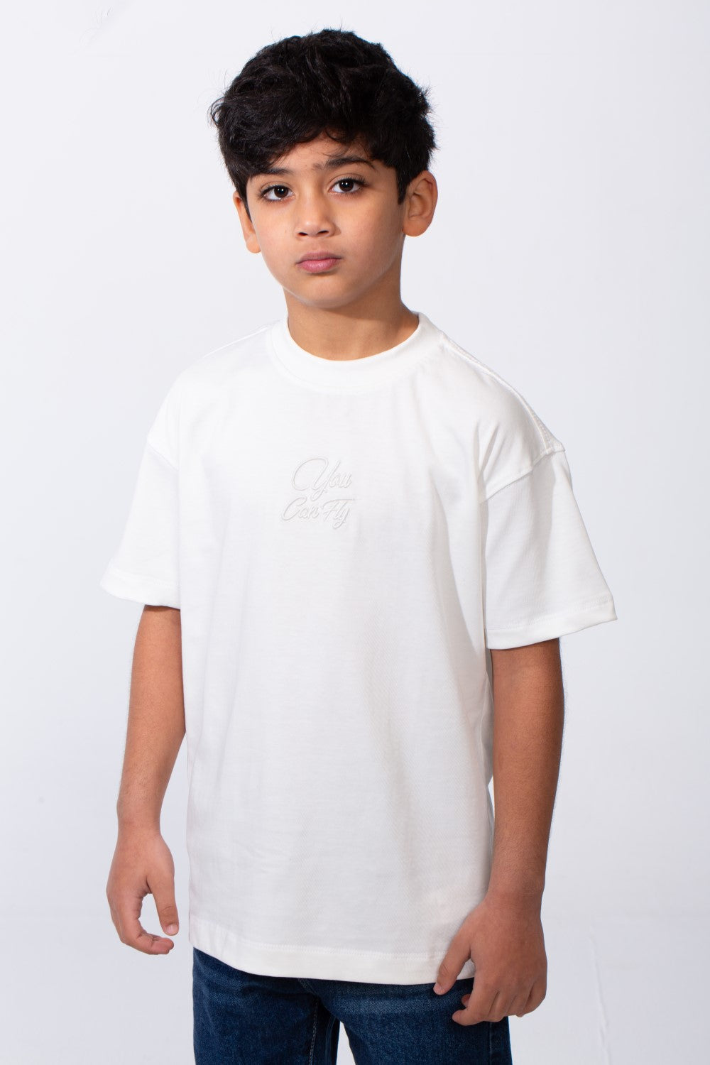 A boy wears a white oversized crew neck t-shirt with subtle typography embroidery on the chest.